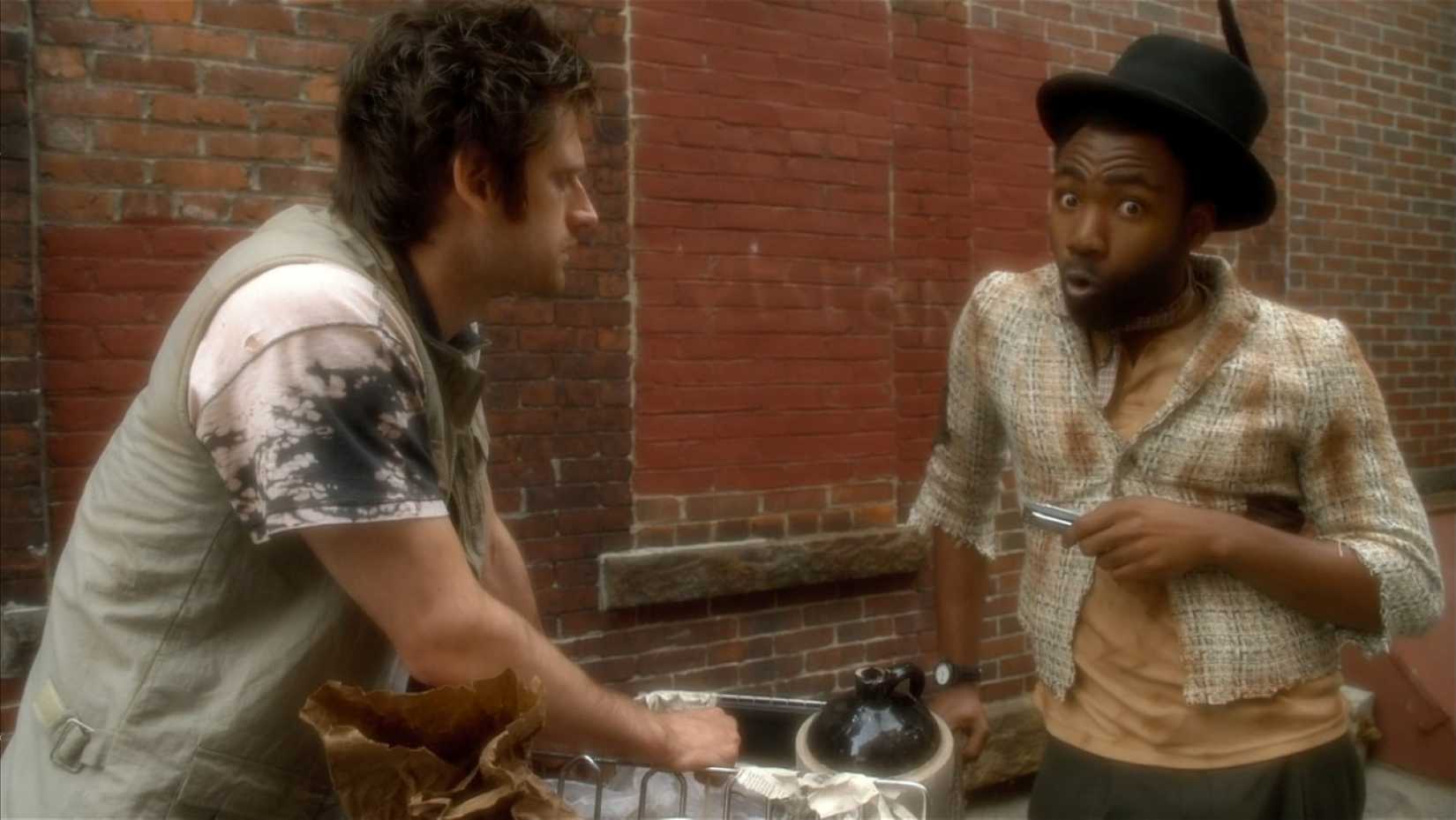 Jason (Donald Glover), a deluded teenager, dresses up as an old-timey hobo with a top hat and harmonica in order to talk to an unhoused person in a scene from Mystery Team.